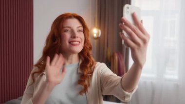 Carefree Kafkasyalı kadın cep telefonu uygulaması el sallayarak evde selamlaşma işareti ile sanal telefon konuşması yapıyor. Gülümseyen kadın video blogu mutlu kız uzaktan konuşmayı çevrimiçi yayınlıyor