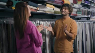 Kumaş dükkanındaki erkek danışman kadın müvekkil Arap erkek satıcı moda tasarımcısı Kafkasyalı kadın müşteri sohbeti atölyedeki tekstil kumaşından bahseden neşeli kız erkek sohbeti.