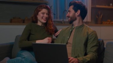 Mutlu, minnettar, beyaz bir kadın, kocasına kanepede sarılıyor, evli çiftler için planlar yapıyor, internette bilet seçiyor, akşam evde bilgisayarla yeni bir online alışveriş yapıyor.