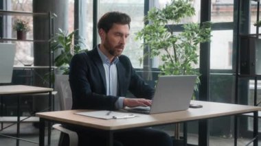 Kafası karışmış Kafkasyalı iş adamı erkek girişimci şirket çalışanı satış müdürü dizüstü bilgisayarda çalışıyor internet yazıları hakkında bilgi arıyor verileri analiz ediyor.