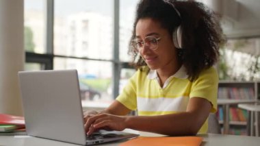Yoğunlaşmış Afrikalı Amerikalı kız öğrenci iş kadını iş kadını iş kadını. Kafede kulaklıklar takıyor. Laptop okulu kütüphanesinde online daktilo bilgisayar eğitimi alıyor.