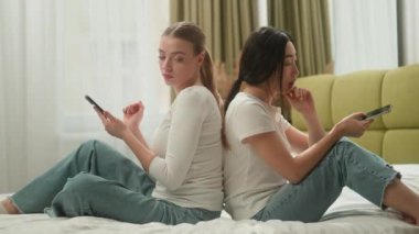 İki çok ırklı kadın arkadaş yan gelip yatmış beyaz kadın Asyalı kadın Koreli kız yatak odasında cep telefonu bağımlılığı olan Z cihazları aşırı kullanımı sorun yaratıyor.