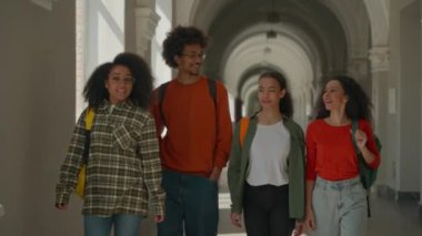Bir grup çok ırklı öğrenci dört farklı arkadaş Afro-Amerikan Latin Latin sınıf arkadaşları erkek erkek, kadın, kız, mutlu bir şekilde gülümsüyor arkadaşça yürüyorlar üniversite koridorunda.