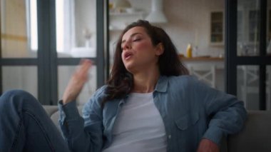 Kanepede aşırı ısınmış beyaz bir kadın. Kanepede el sallıyor. Kolları yorgun, terli bayan.
