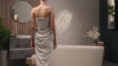 Beyaz pamuklu havluya sarılı beyaz kadın kadın kadın banyo için hazırlanıyor banyo küvetinde yıkanmaya hazır ev banyosu güzellik prosedürü vücut bakım rutini dinlendirici spa