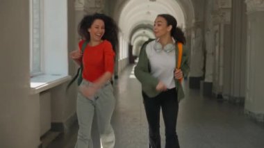 İki mutlu aktif öğrenci, gülümseyen kızlar, gülümseyen kadın arkadaşlar, Latin kökenli çok ırklı kadınlar, akademi üniversitesinde ders çalışmak için acele ediyorlar.