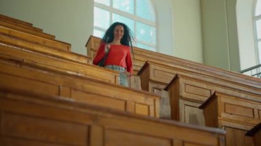 Gülümseyen kız öğrenci, sırt çantalı Latin bayan. Üniversite kolejine geliyor. Büyük boş oditoryum.