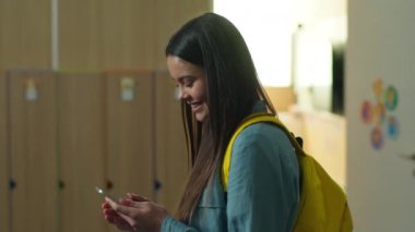 Gülümseyen mutlu beyaz kız öğrenci kız öğrenci kız öğrenci okul koridorunda yürüyen üniversite koridorunda eğitim gören akıllı telefon bağımlısı.