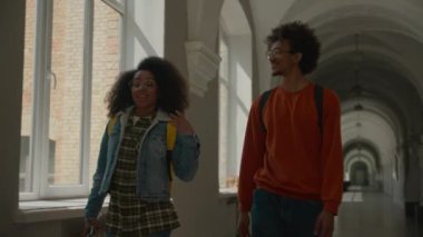Afro-Amerikan gülümseyen adam, erkek, kız kadınla konuşan erkek, iki öğrenci arkadaşı, iki kardeş, iletişim eğitimi hakkında konuşuyorlar, koridor koridorundaki üniversite kolejine gidiyorlar.