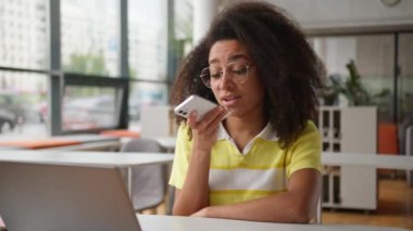 Mutlu Afrikalı Amerikalı kız öğrenci, iş kadını, hoparlörden konuşan, akıllı telefon konuşan, akıllı telefon, kafede dizüstü bilgisayarlı üniversite kütüphanesiyle sesli mesaj kaydeden.