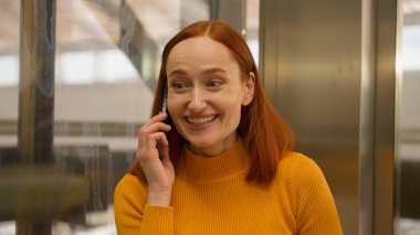 Neşeli, beyaz, genç, bayan, iş kadını, arkadaş canlısı cep telefonuyla konuşan, indirimli, asansörlü, asansörlü, asansörlü, kapalı alışveriş merkezindeki asansörü terk eden kadın.