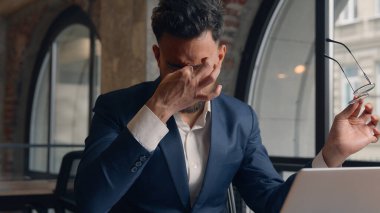 Arap Hintli iş adamı erkek işadamı ofiste dizüstü bilgisayar başında çalışan erkek baş ağrısı çekiyor migren gözlüğü çıkarıyor kaşınan gözler gergin bulanık görme yorgunluğu yorgun aşırı çalışma sağlık sorunu