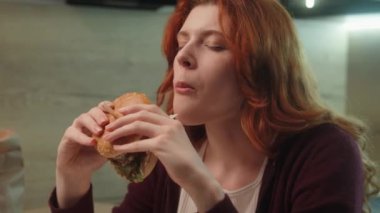 Kafkasyalı genç bayan müşteri abur cubur yiyen hamburger çiğneyen çizburger yiyen yemek diyeti yiyen ev ortamında cezbedici yemek yiyen. Sağlıksız abur cubur, aşırı kalori tüketimi.