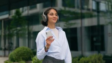 Kablosuz kulaklıkla müzik dinleyen mutlu gülümseyen bayan. Cep telefonu uygulaması. Şehirde yürüyen Afro-Amerikan öğrenci kız iş kadını.
