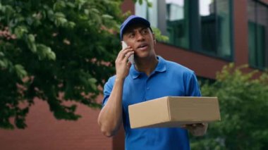 Müşterilerle telefon görüşmesi akıllı telefon görüşmesi açık hava Afrikalı Amerikan kurye teslimatçı erkek teslimatçı servis elemanı alışveriş paketi karton paket siparişi şehir sevkiyatı postacısı