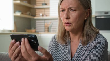 Şok olmuş 70 'li yaşlarda emekli yaşlı, yaşlı, yaşlı, kadın, cep telefonlu, cep telefonlu bir büyükanne. Mesajı okudu.