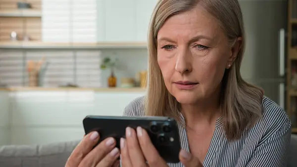 stock image Shocked anxious 70s retired senior Caucasian woman elderly female grandmother looking mobile phone cellphone pensioner read message getting bad scam notification bank debt health medical problems home