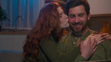 Mutlu gülümseyen beyaz evli çift evde romantik bir akşam geçiriyorlar sosyal ağda takılıyorlar tatil rezervasyonları yaptırıyorlar film izliyorlar dizüstü bilgisayar eşleri kocalarına sarılıyorlar.