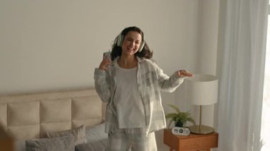 Yatak odasında dans eden neşeli kadın ev telefonunun keyfini çıkar. Neşeli kulaklıklar, müzik dinleyen kadın teknolojisi. Mutlu heyecan verici enerji eğlencesi.