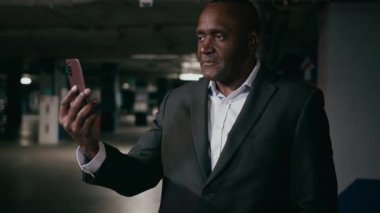 Ciddi bir Afrikalı Amerikalı iş adamı akıllı telefon ile konuşuyor. Erkek girişimci iş adamı internet konferansında iletişim kuruyor. Yeraltı otoparkında uzaktan telefon görüşmesi yapıyor.