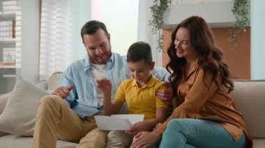 Heyecanlı, mutlu, beyaz bir aile babası, anne-baba-oğul. Evinde, kanepe başında, çocuk iyi haberler okuyor. Zaferi kutluyor.