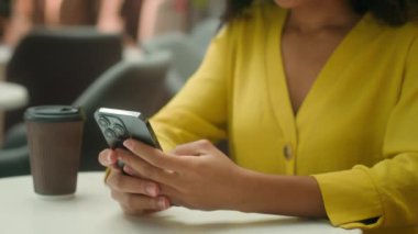 Kapalı ellerde akıllı telefon cep telefonu tutan Afrikalı Amerikalı kadın internetten mesaj atıyor müşteri müşterisi müşterisi kız gülüşü kahve sohbetinden keyif alıyor.