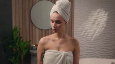 Banyo havlusuna sarılı beyaz, mutlu, gülümseyen bir kadın. Kız banyosu, duş jeli şampuan, saç kremi, kozmetik losyon, baş parmak yukarı.