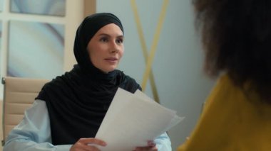 İki iş ortağı kadın, tesettürlü Müslüman kadın iş kadını, emlakçı. Ofis toplantısında Afrikalı kadın müşteriye danış. Sözleşme imzası, belge, müzakere ortaklığı anlaşmasını tartış.