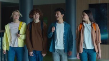 Mutlu gülümseyen Kafkasyalı dört arkadaş, öğrenciler, gençler, kızlar, erkekler koridorda yürüyen erkekler, okul üniversitesinde arkadaşça konuşmalar.