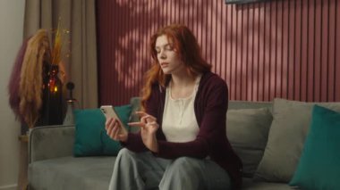 Kanepede cep telefonu kullanan kadın. Kafkasyalı, karnı ağrıyan, karnı ağrıyan, açlık çeken, yemek siparişi veren, marketten alışveriş yapan, internetten cep telefonu alan.
