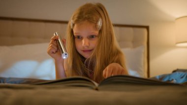 Meraklı beyaz çocuk kitap okuyacak ders kitabı okuyacak kız yatakta yatacak ev ödevi eğitimi alacak elinde fenerle gece yatak odası tutan çocuk çalışacak.