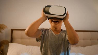 Komik hevesli çocuk okul çocuğu yenilikçi dijital VR gözlükler kullanarak video oyunu oynuyor. Meta-evren dünyasında 3D AR teknolojisi kullanıyor. Evde yatağın üzerinde sanal gerçeklik gözlüğü takıyor.