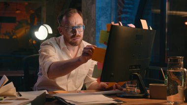 Kafkasyalı iş adamı, iş adamı, karanlık gece ofis çalışanı. Çıkartmalar hakkındaki çek bilgilerini okuyor. Tatminsiz kağıt parçalarını bilgisayar ekranının son teslim tarihine kadar çöpe atıyor.