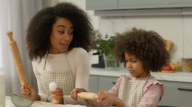 Afro-Amerikan aile şefkatli anne anne anne anne küçük kız çocuğa yemek pişirmeyi öğretiyor un buğday buğdayını gösteriyor yumurta gösteriyor merdaneyi veriyor mutfakta konuşan aşçıyı nasıl kullanacağını açıkla.