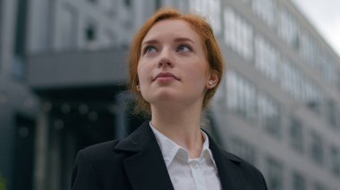 Kendine güvenen, başarılı, genç, beyaz, kızıl saçlı, mutlu, iş kadını, zarif, resmi giyinmiş, şehir merkezindeki kameraya benzeyen bir kız. İş başarısı hedefleri