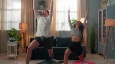 Aktif evli genç çift spor ailesi İspanyol kadın fitness kızı karısı ve beyaz adam erkek antrenör koca kaslarını esnetiyor egzersiz yogası yapıyor oturma odasında Asana 'ya poz veriyor