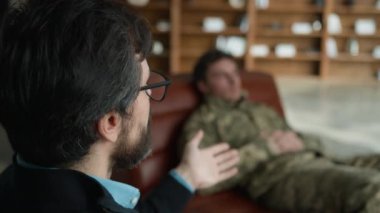 Orta yaşlı Kafkasyalı psikolog erkek, subay kamuflaj üniformalı asker ile konuşuyor. Kanepede yatıp psikiyatrist danışma odasında yatan hastayı bulanıklaştırıyor.
