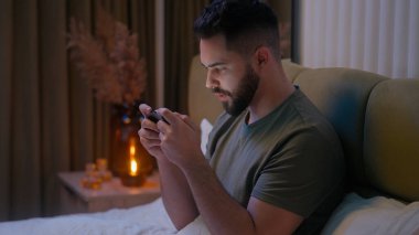 Kafkasyalı bir adam cep telefonu akıllı telefon aleti kullanıyor online sanal oyun oynuyor tutkal bağımlısı erkek adam akşam dijital cihaz siber dinleme bağlı elektronik yatak odası