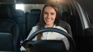 Kiralık arabanın içinde oturan beyaz kadın şoför. Kameraya mutlu bir şekilde gülümsüyor. Yeni bir araba satın alırken gülümsüyor.