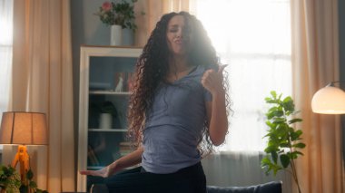 Şok olmuş mutlu İspanyol etnik kadın gülümseyen bayan sporcu kız eski büyük kot pantolon giyiyor zayıflama başarısının tadını çıkarıyor kamera karşısında baş parmak hareketi gösteriyor.