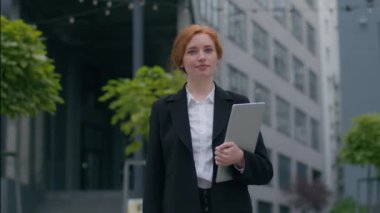 Başarılı özgüven sahibi beyaz iş kadını kadın kadın çalışan iş kadını proje yöneticisi elinde dizüstü bilgisayarla şehir merkezindeki ofisin önünde kameraya poz veriyor.