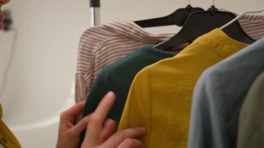 Moda modasına uygun giyinmeyi seçen beyaz kadın moda moda blogu iş için hazırlanıyor blogcu kız blogcuları alıyor stüdyodaki askıların dolabından yeşil gömlek alıyor.