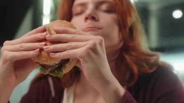 Kafkasyalı mutlu kadın müşteriler çiğnenmiş lezzetli hamburgerler yiyorlar. Lezzetli hamburgerler yiyorlar. Kapalı mutfak odasında çizburger çiğnemenin tadını çıkarıyorlar. Fast food dağıtımı sağlıksız beslenme