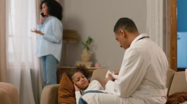 Afrika kökenli Amerikalı anne cep telefonuyla konuşuyor. Doktor çocuk doktorunu arıyor. Sıcaklığı ölçüyor.