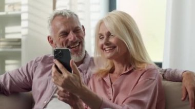 Mutlu aile yaşlıları, 50 'li yaşlarda, Kafkasyalı yaşlı kadın, erkek, erkek, video konuşuyor, gülümse. Büyükanneler cep telefonu uygulaması kullanıyor. İnternet üzerinden alışveriş yapma konusunu tartışıyorlar.