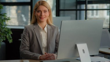 Gülümseyen orta yaşlı kadın işkadını iş yerinde bilgisayar başında mutlu yönetici kadın işveren kadın profesyonel yönetici portresiyle poz veren kamera tebessümüne bakıyor.