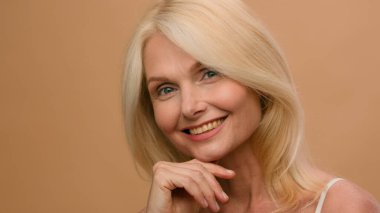 Bej renkli fotoğraf stüdyosu, olgun orta yaşlı mutlu kadın 50 'li yaşlarda model beyaz kadın yüzü cilt bakımı lüks anti-yaşlanma kozmetikleri kolajen tıbbi kırışıklık önleyici doğal makyaj.