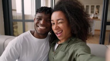 Mutlu, sevecen bir çift, etnik Afro-Amerikan aile fotoğraf cep telefonuyla evde gülümseyen selfie kameralı, kadın, erkek, erkek, kadın blogcu, video blogcuları etkiliyor.