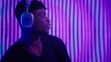 Dans eden siber uzay Afrikalı Amerikalı kulaklıklı adam neon yeniliğindeki müzik sesi kalitesini dinliyor menekşe mavisi fütüristik stüdyo klübü fütürizmcisi erkek dans ediyor.