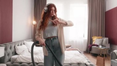 Neşeli, komik, beyaz, kadın, ev hanımı, ev hanımı, elektrikli süpürge temizleyicisi, dağınık yatak odasında gitar dansı yapıyor, yerleri süpürüyor, müzik kulaklıkları dinliyor.